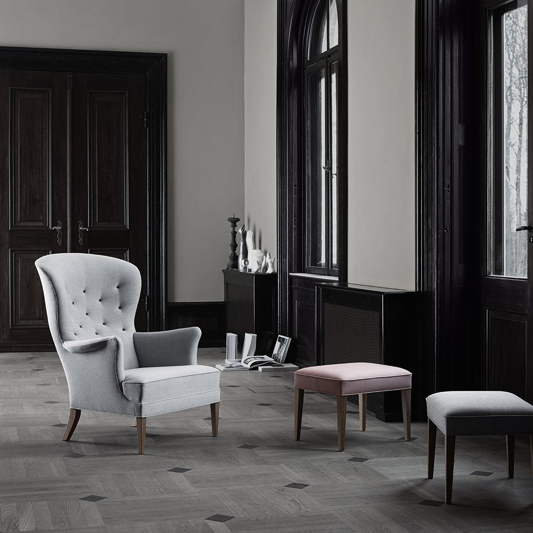 Gray tufted armchair and pastel pink and white stools in a modern, elegant room with dark wood accents and light flooring.