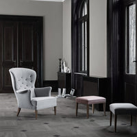 Gray tufted armchair with light pink and white upholstered stools against a dark wood and gray backdrop.