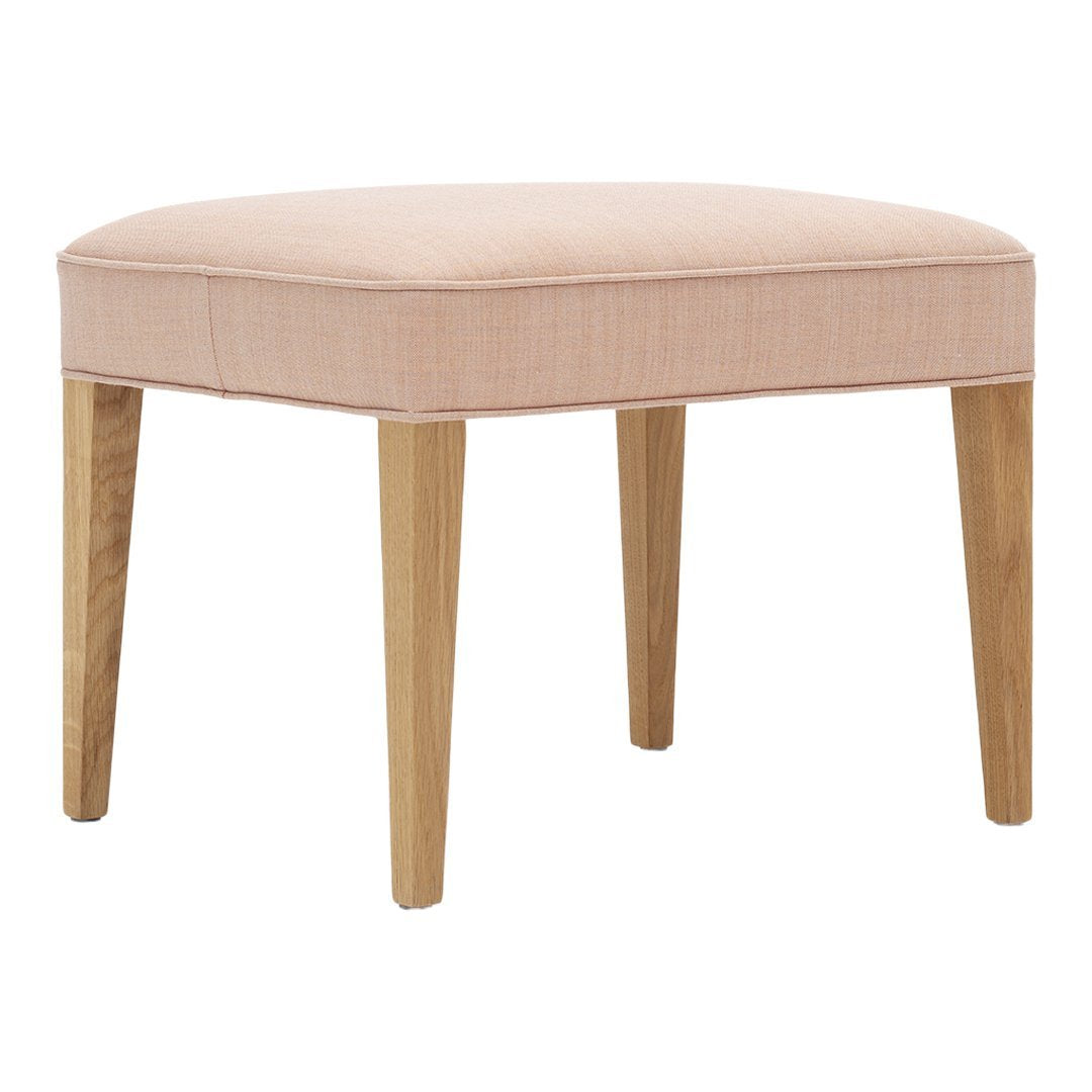 Soft pink upholstered ottoman with natural wood legs, featuring a simple, contemporary design.