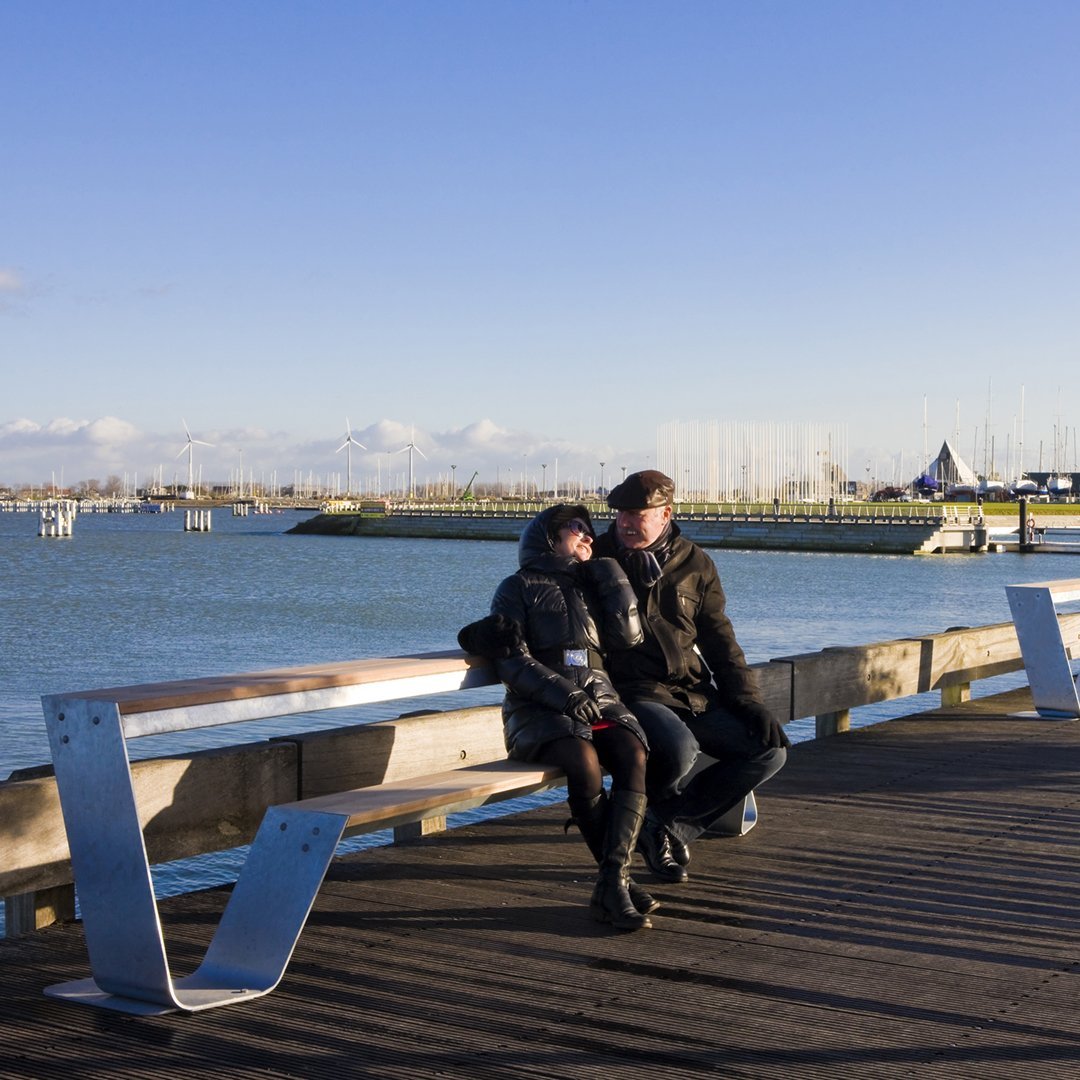 Two individuals in dark coats against a serene blue sky, with a subtle water pattern and wooden boardwalk.