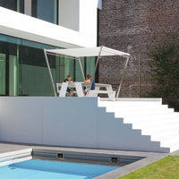 Modern white patio with a sleek canopy, featuring clean lines and vibrant green grass beside a clear blue pool.