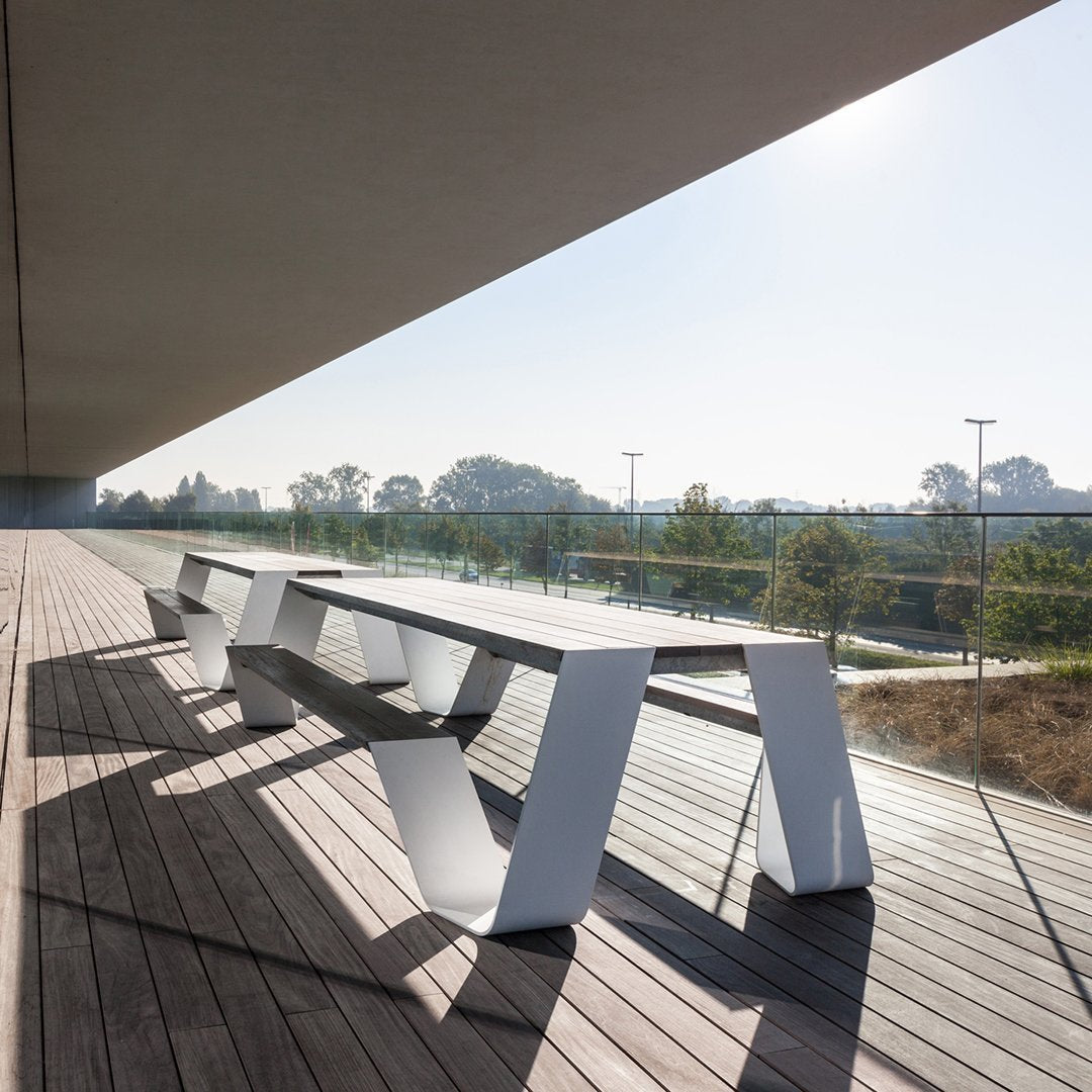 Modern white outdoor dining table with sleek lines, contrasted against a wooden deck and green nature backdrop.