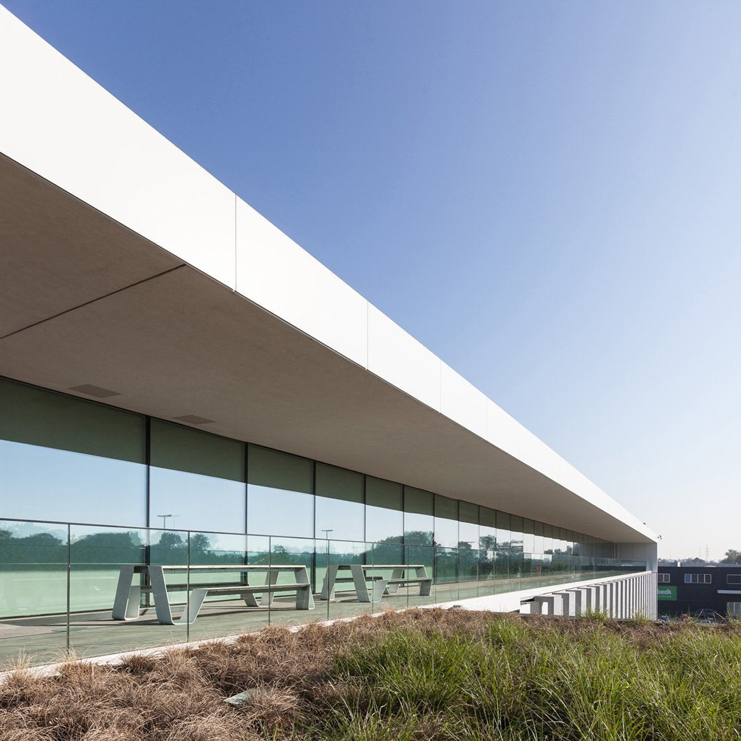 Sleek white architectural lines with clear glass and blue sky; green grass accents in the foreground.