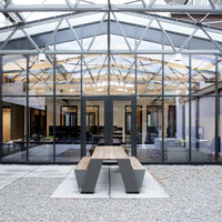 Modern outdoor table with a gray finish and sleek angular design, set against a glass and metal structure.