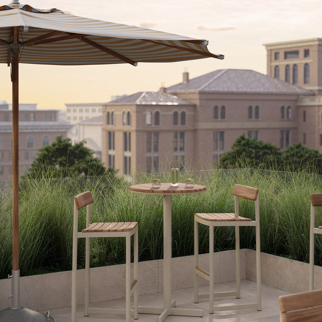 "Light beige bar stools with natural wood accents under a striped cream and beige umbrella on a chic patio setting."