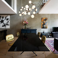 "Modern black dining table with gold-accented chairs and floral centerpiece, set against an eclectic patterned rug."