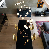 Black dining table with golden chairs, modern light fixtures, and a colorful patterned rug on a wooden floor.
