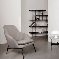 "Modern gray armchair with a minimalist design, set against a light backdrop and black shelving unit."