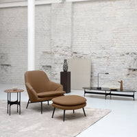 Brown upholstered chair and ottoman with black furniture accents and a neutral-toned rug in a minimalist setting.