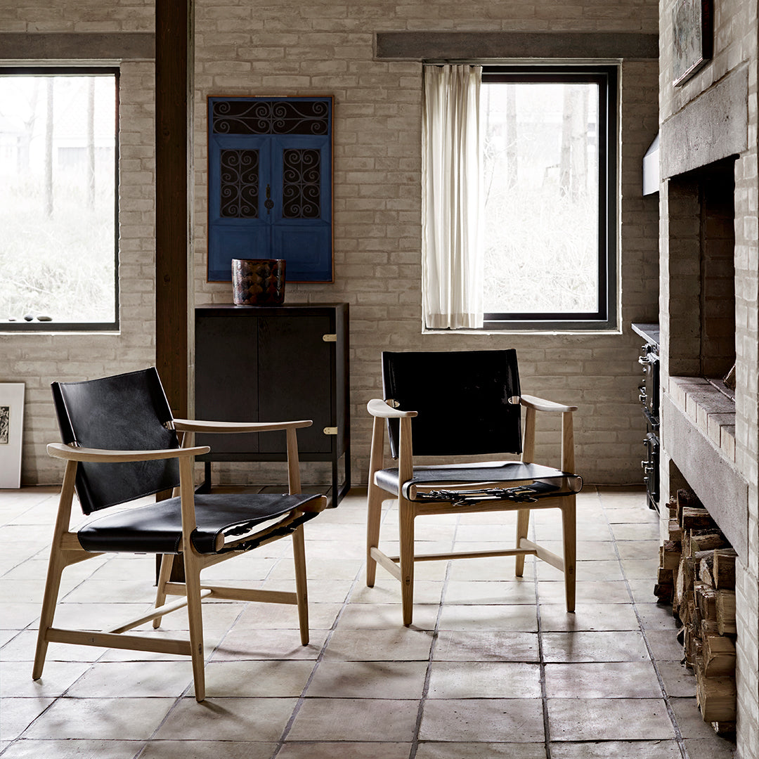 "Mid-century modern chairs with black leather seats and wooden frames, set against a neutral-toned, rustic interior."