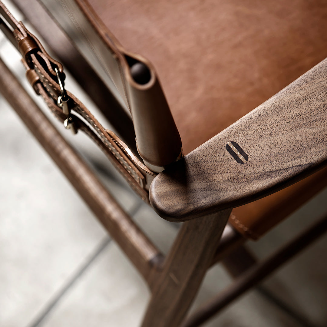 "Close-up of a walnut wood chair frame with rich brown leather accents and minimalist design details."