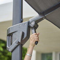Gray metal crank mechanism for a retractable awning with a dark, textured fabric overhead. 