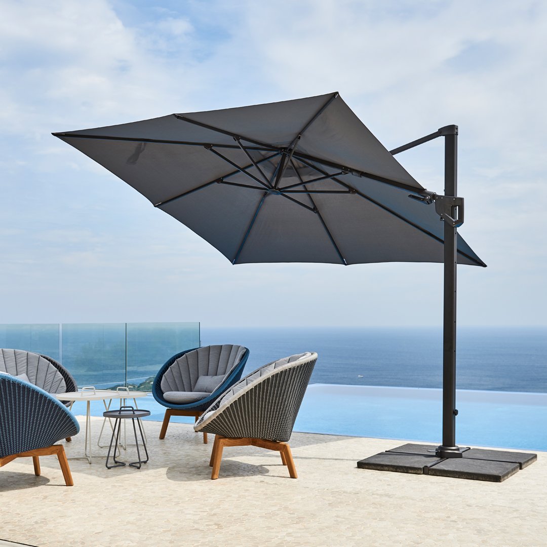 Large black patio umbrella with a sleek design, surrounded by gray and blue accent chairs against a serene ocean backdrop.
