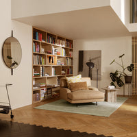 "Modern living room with beige sofa, green rug, wooden shelves, and circular mirror in a warm, neutral palette."