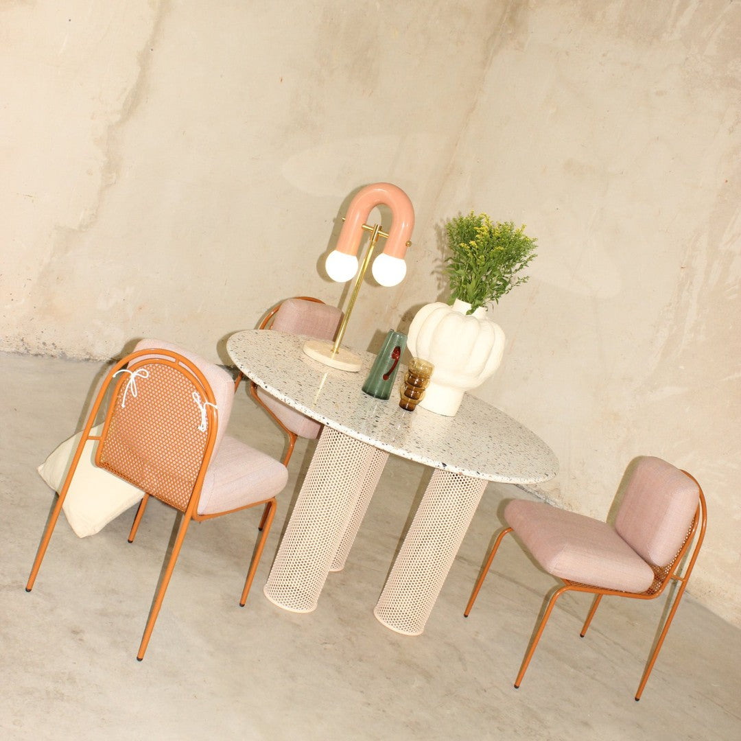 Light pink chairs and a speckled round table with a textured base, complemented by soft pastel accents.