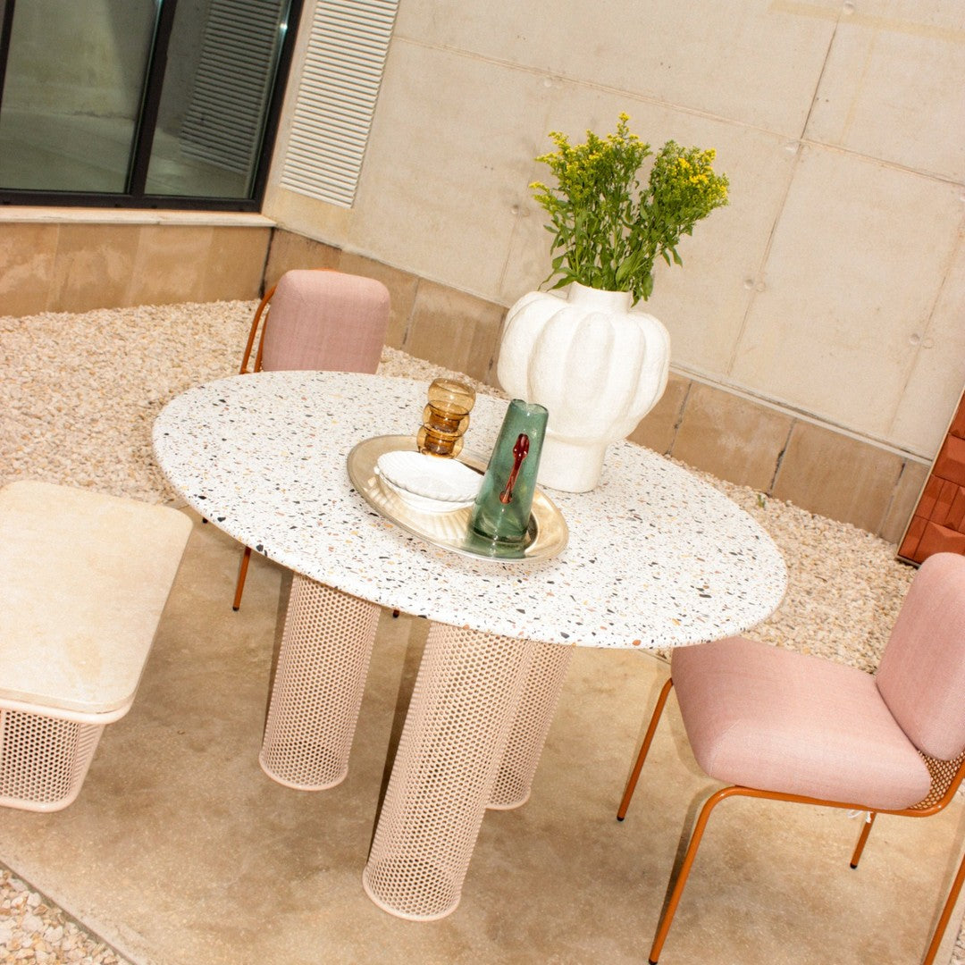 Round white terrazzo table with pastel pink chairs and transparent legs, featuring natural texture and elegant decor.