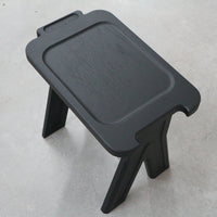 Black folding stool with a smooth surface and clean edges, featuring a minimalist design for versatile use.