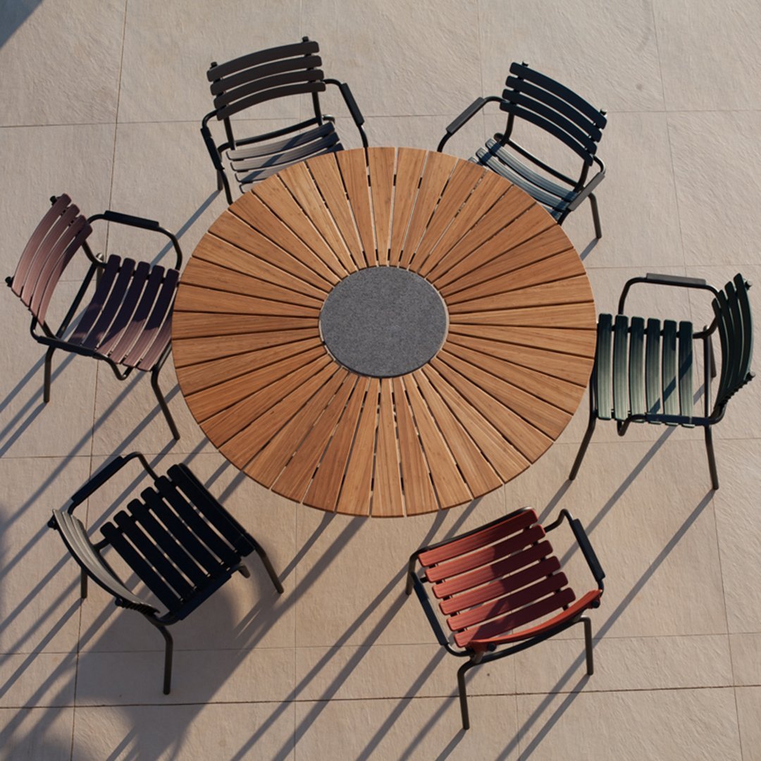 Circular wooden table surrounded by striped chairs in shades of green, pink, and black. Elegant outdoor dining set.
