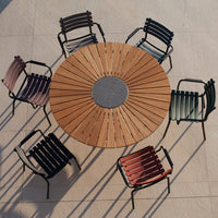 Circular wooden table surrounded by striped chairs in shades of green, pink, and black. Elegant outdoor dining set.