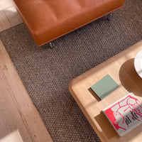 "Brown woven rug under a light wood table, complemented by orange leather armchair and colorful books."
