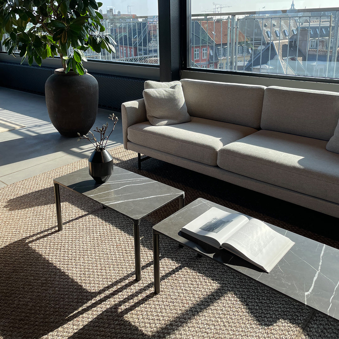 "Modern living room with gray marble tables, beige sofa, and natural woven rug, enhanced by sunlight."