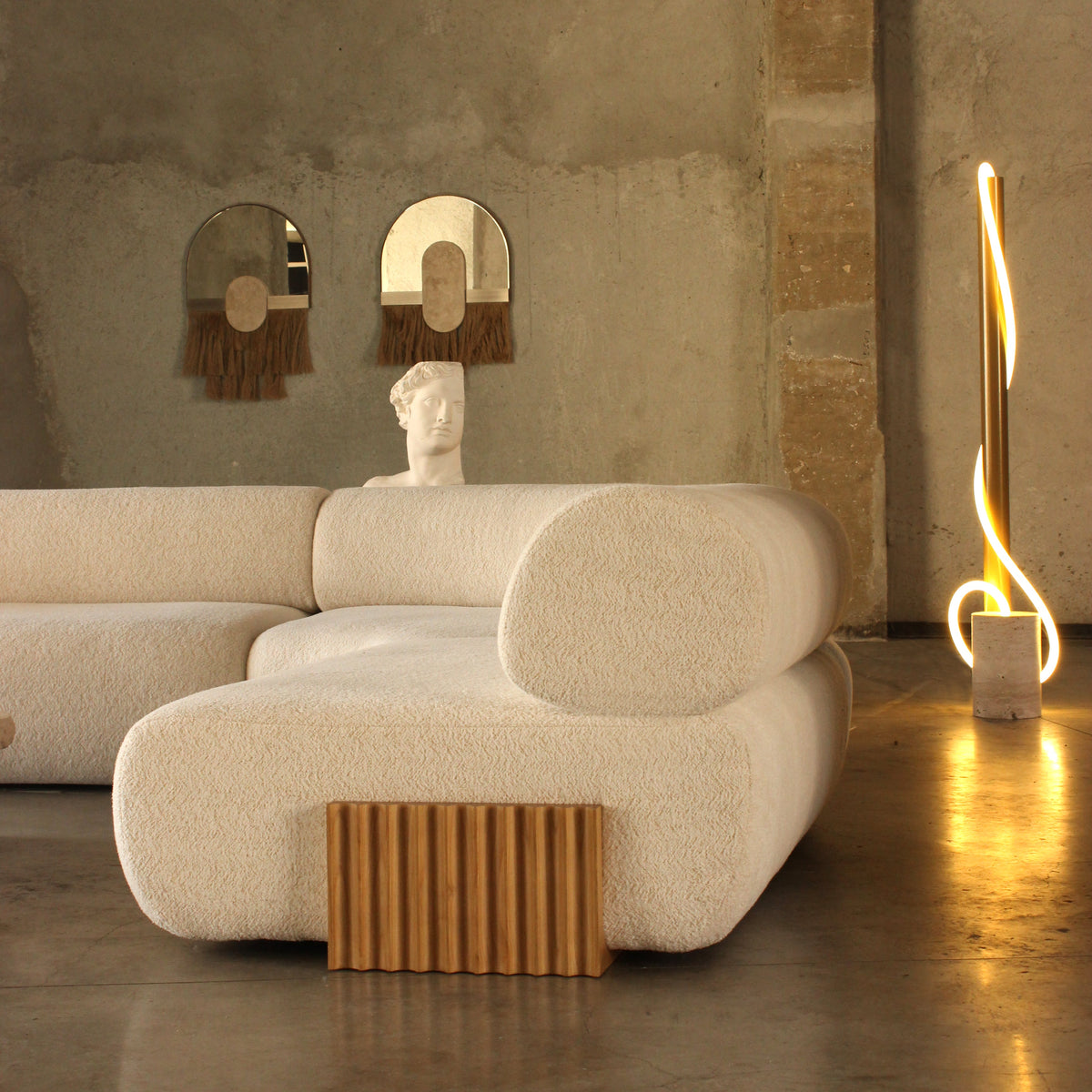 Stylish beige sofa with textured fabric and wooden accent, set against a minimalist, neutral-toned interior.