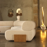 Stylish beige sofa with textured fabric and wooden accent, set against a minimalist, neutral-toned interior.
