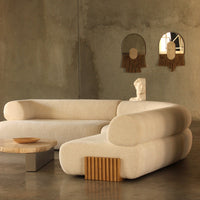 Cream-colored, textured sofa with rounded edges and wooden accents, set against a minimalist gray backdrop.