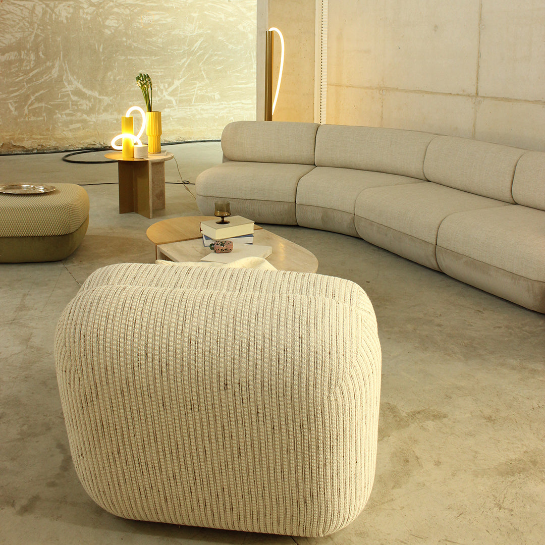 Beige ribbed pouf with a textured pattern, paired with a soft beige curved sofa in a contemporary interior setting.