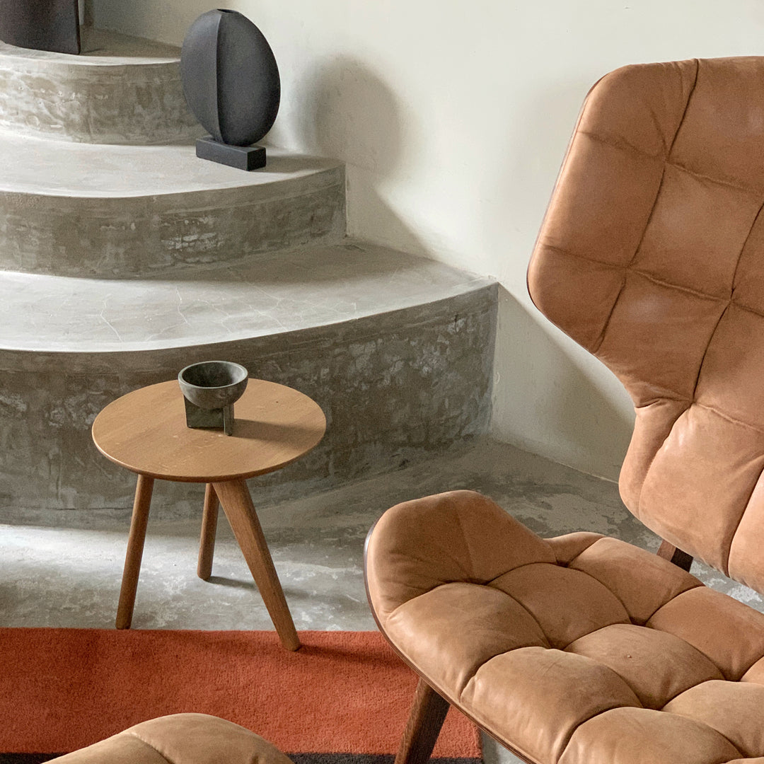 Tan leather chair, round brown side table, and orange rug on a concrete staircase. Modern, minimalist interior colors.