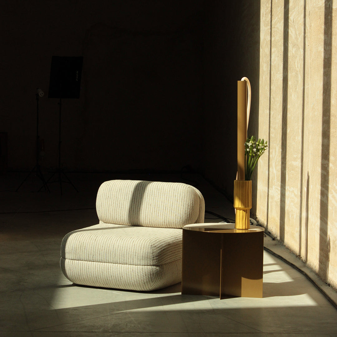 Light beige ribbed sofa with grey accents beside a gold side table and warm yellow vase. Soft, modern aesthetic.