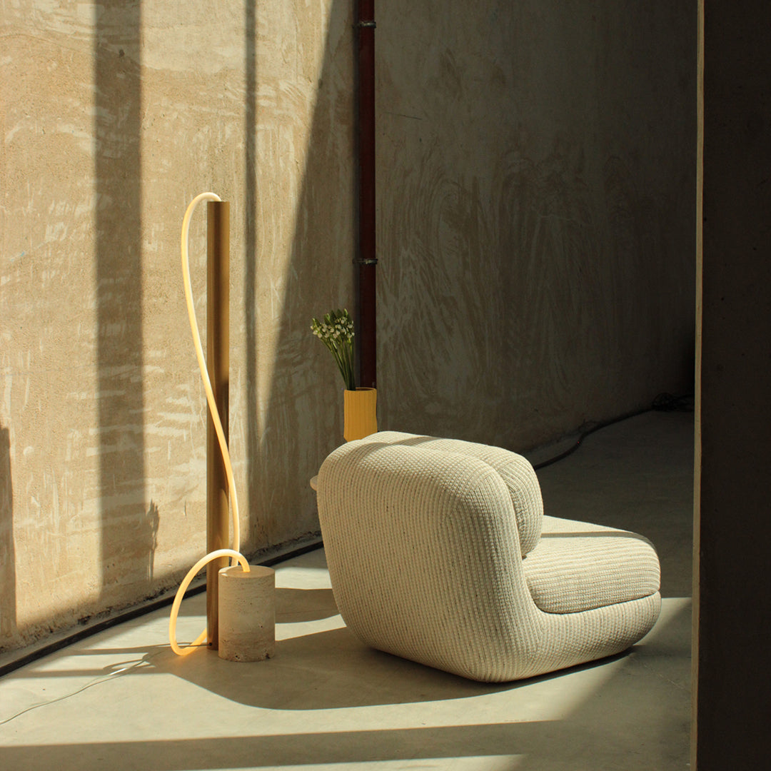 Textured beige chair with soft cream accents, paired with a light yellow lamp and subtle green plant in a minimalistic interior.