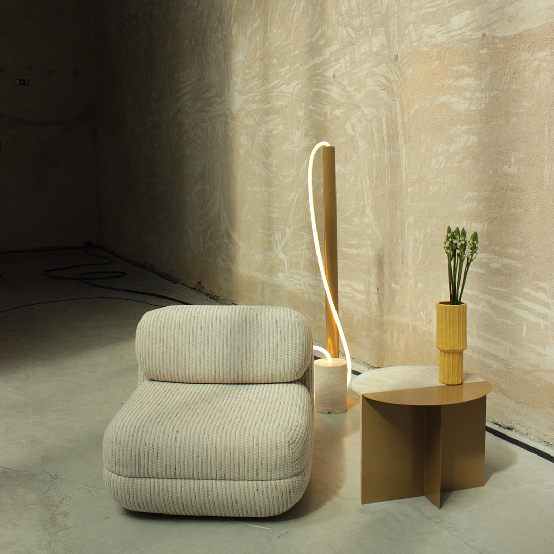Textured beige sofa with striped pattern, golden lamp, and yellow vase on a minimalist table in a neutral environment.