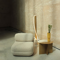 Textured beige sofa with striped pattern, golden lamp, and yellow vase on a minimalist table in a neutral environment.