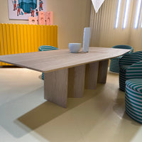 Contemporary wooden table with light oak finish, paired with striped teal and white chairs in a bright yellow setting.