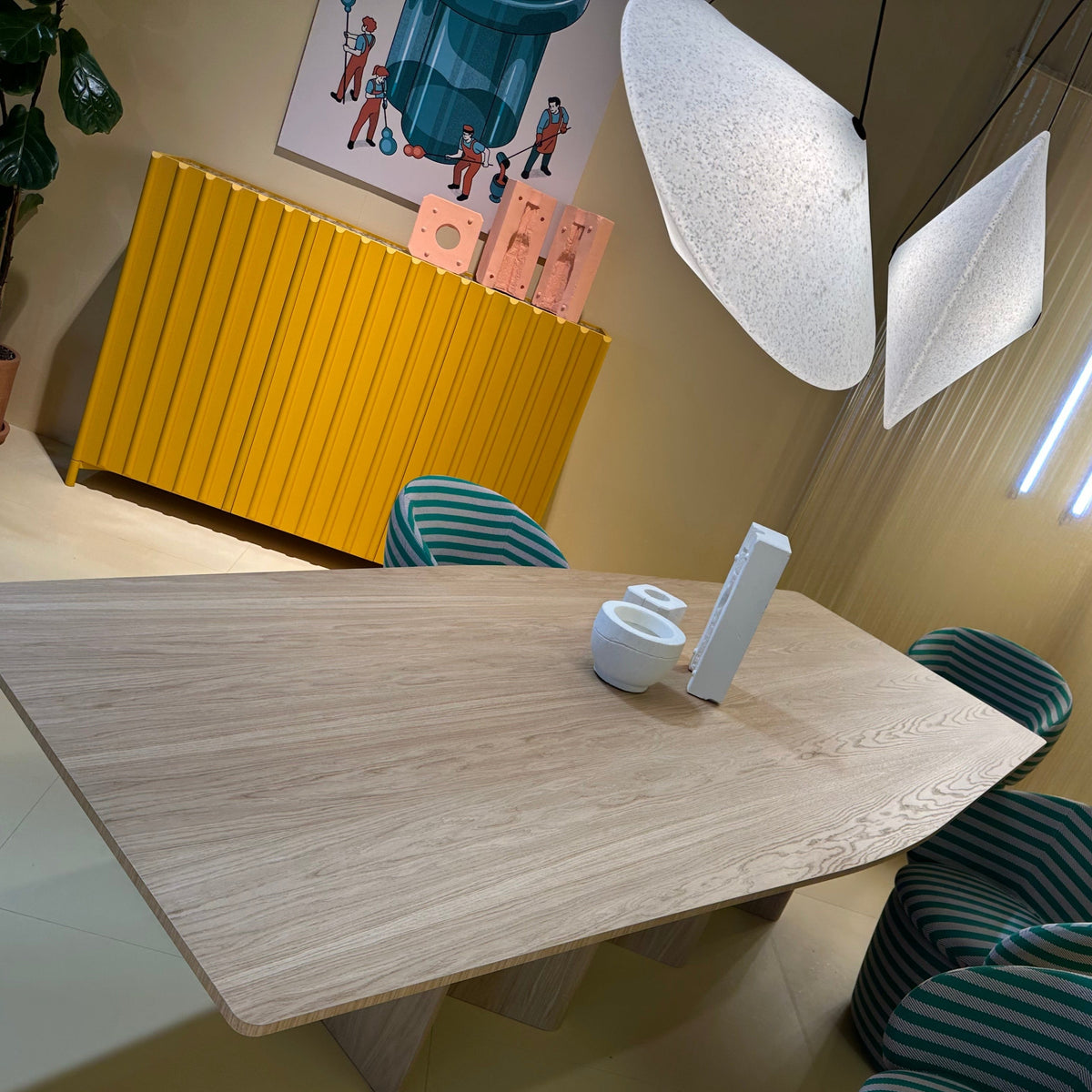 Light wood dining table with green striped chairs, bright yellow cabinet, and soft white light fixtures.