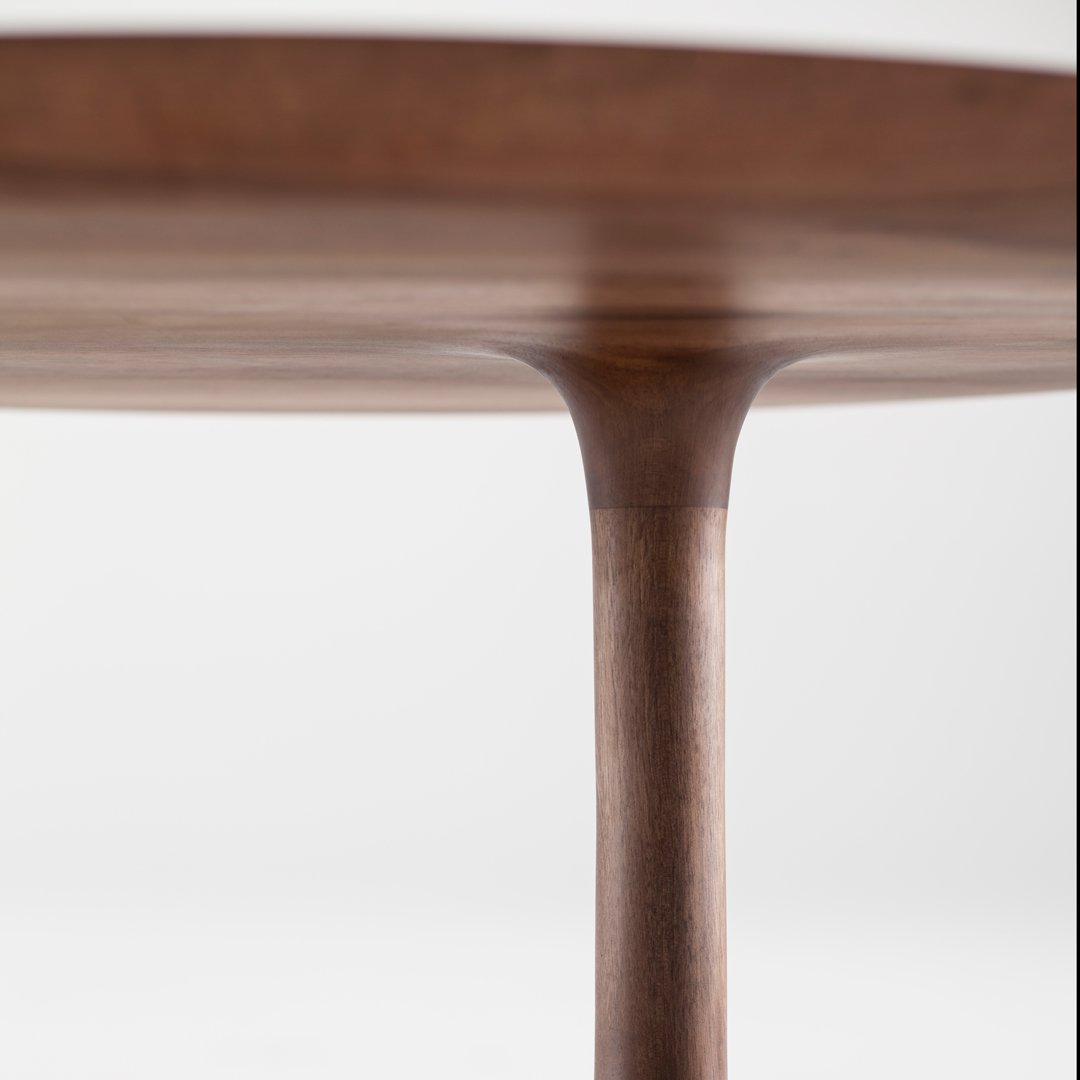 Round walnut table with a smooth finish and natural wood grain pattern, showcasing rich brown tones and elegant design.