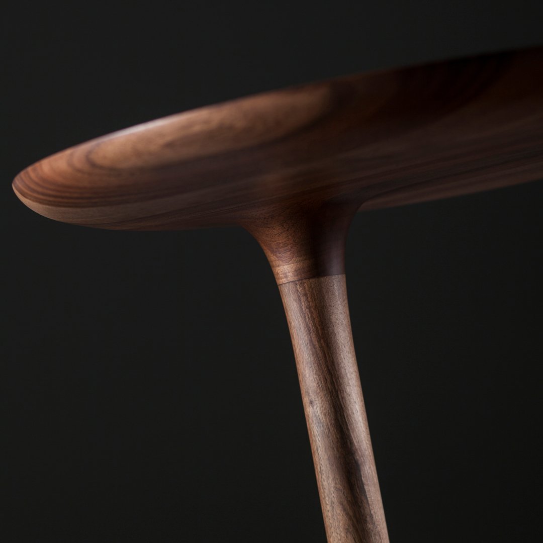 Elegant walnut tabletop with a smooth finish and tapered legs against a dark background, showcasing natural wood grain patterns.