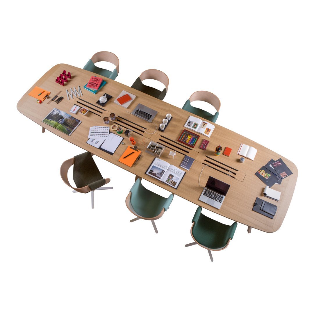 Modern wooden table with light oak finish, paired with green and beige chairs. Art supplies and books arranged on top.