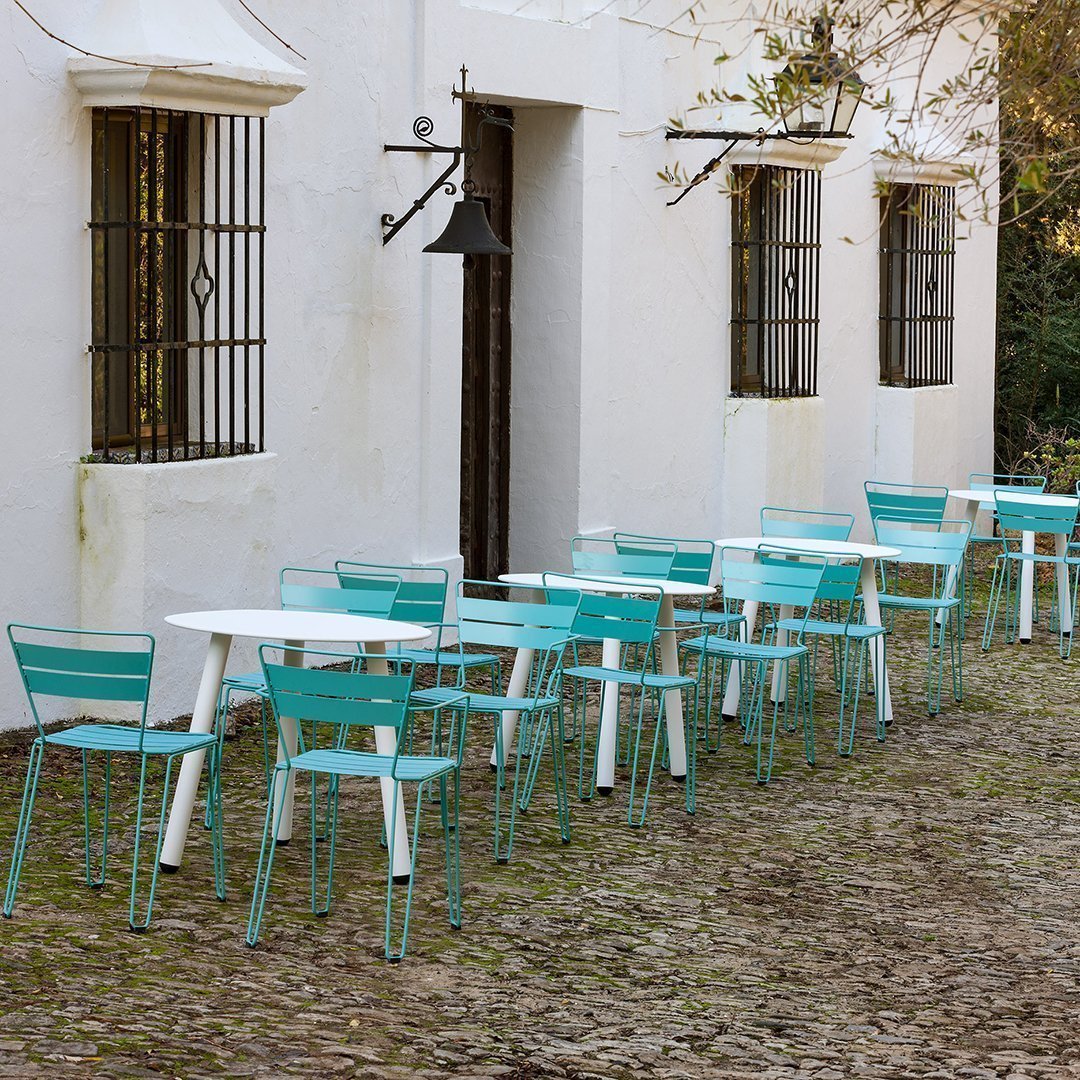 Turquoise metal chairs and tables against a white building, set on a rustic cobblestone patio.