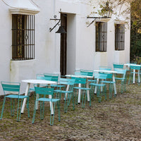 Turquoise metal chairs and tables against a white building, set on a rustic cobblestone patio.