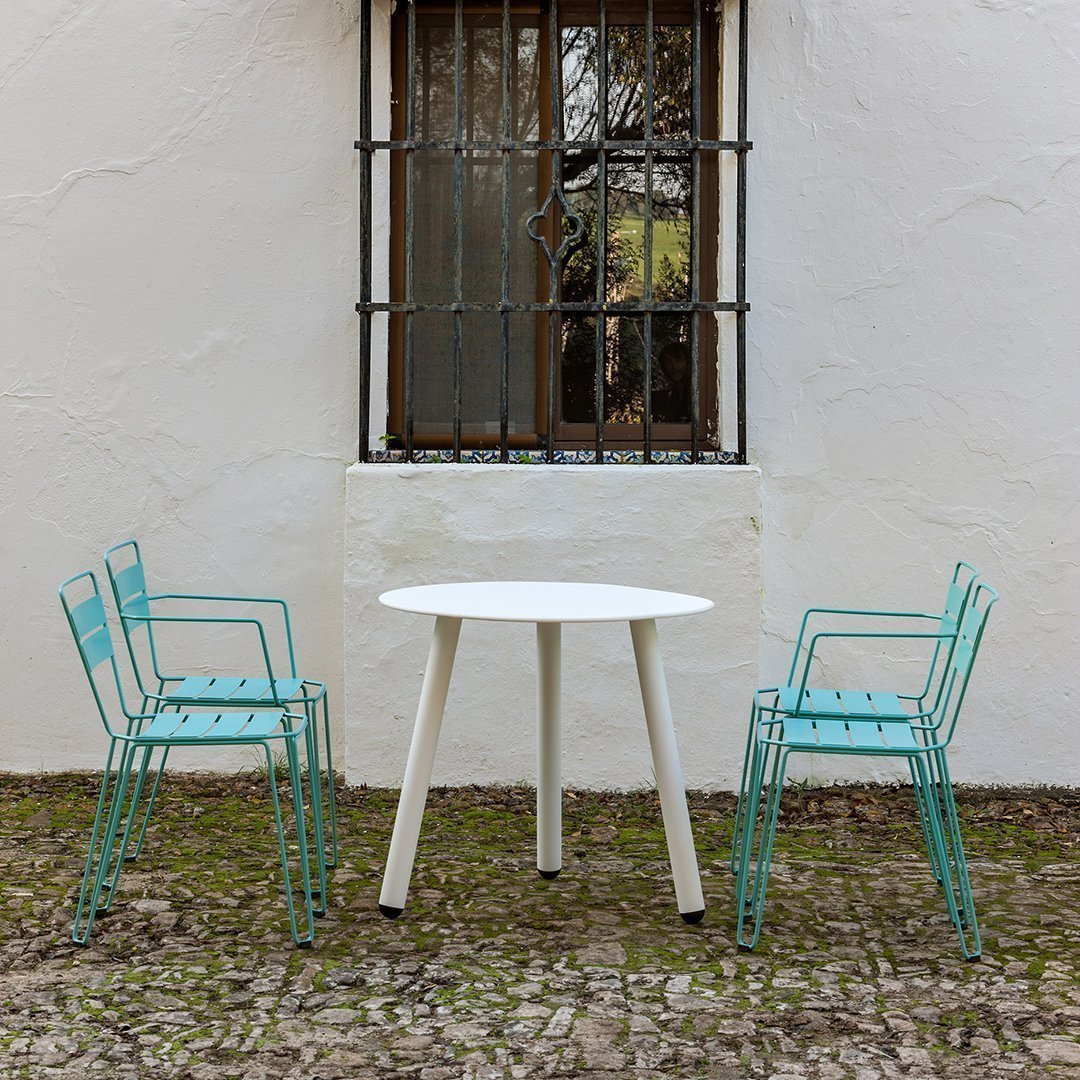 A modern white round table with aqua blue patterned chairs in a rustic outdoor setting.