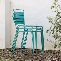 Stacked teal metal chairs against a neutral wall, featuring a sleek, modern design with clean lines.
