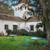 Colorful outdoor chairs in vibrant blue and red, set against lush green grass and a whitewashed building backdrop.