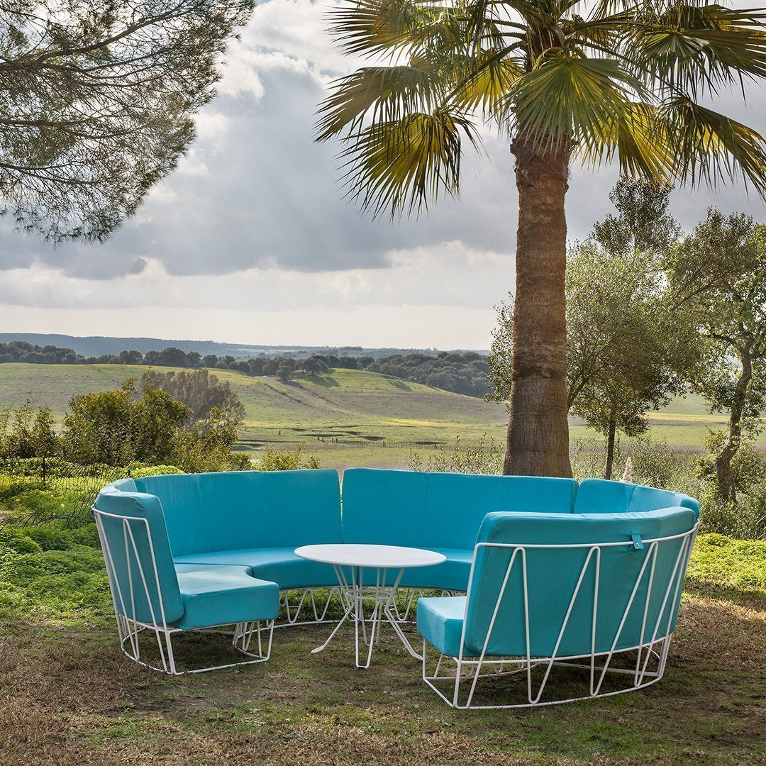 Turquoise sectional sofa with geometric white frame, set in a lush green outdoor landscape.