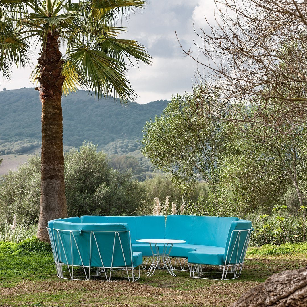 Vibrant turquoise sectional sofa with sleek silver accents, set against a natural green landscape. Perfect for outdoor spaces.
