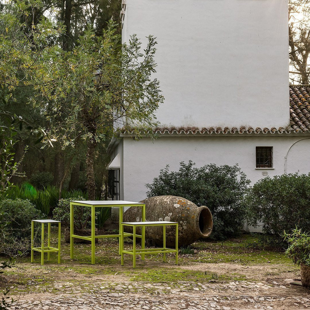 "Vibrant green outdoor furniture set against a neutral white wall and earthy tones of stone and greenery."