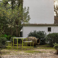 "Vibrant green outdoor furniture set against a rustic white wall and natural greenery."