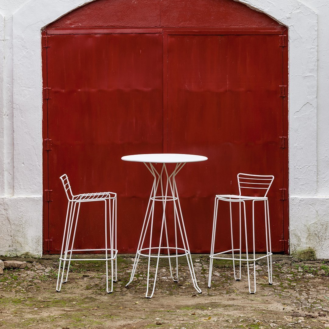White wire bar table and stools against a rustic red background, featuring modern minimalist patterns.