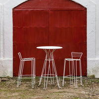 White wire bar table and stools against a rustic red background, featuring modern minimalist patterns.